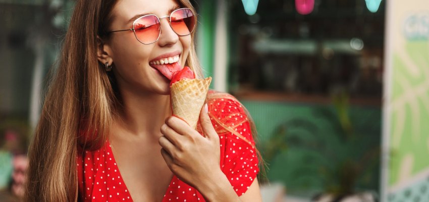 Happy young woman eating sweets on summer vacation. Female traveller licking ice cream and enjoying tropical paradise, explore city and local cuisine.