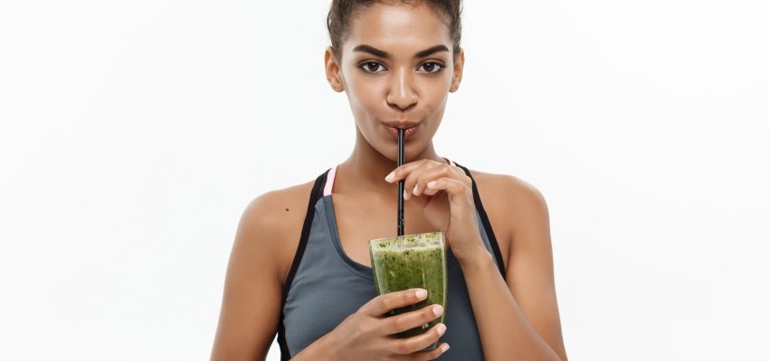 Healthy and Fitness concept - Beautiful American African lady in fitness clothing drinking healthy vegetable drink. Isolated on white background