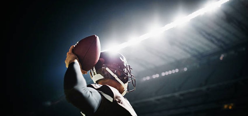 Professional football quarterback preparing to throw pass on stadium field at night